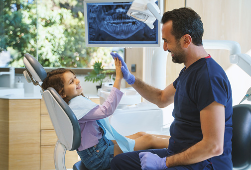 Close up portrait of a male dentist giving a high five to little girl at dental clinic