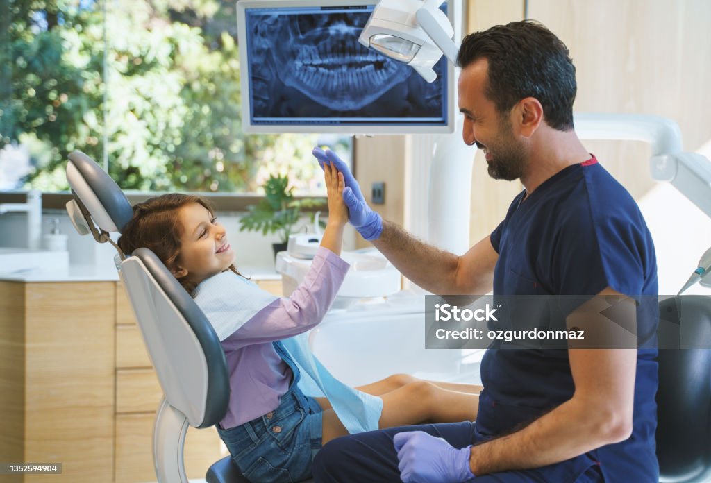 Close up portrait of a male dentist giving a high five to little girl at dental clinic Dentist Stock Photo