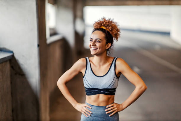 istock A happy fit urban runner is standing under the underpass with her hands on hips and smiling. The effort is always worthy if you have a goal. An urban runner resting. 1352597141