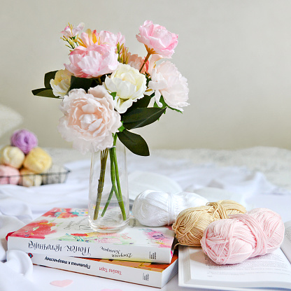 Spring flowers in a vase on the bed, skeins of yarn and books