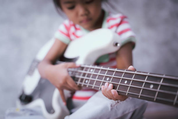 asiatische mädchenhand, die eine 4-saitige bassgitarre mit einem weißen farbkörper hält (fokus auf finger) - bass guitar stock-fotos und bilder