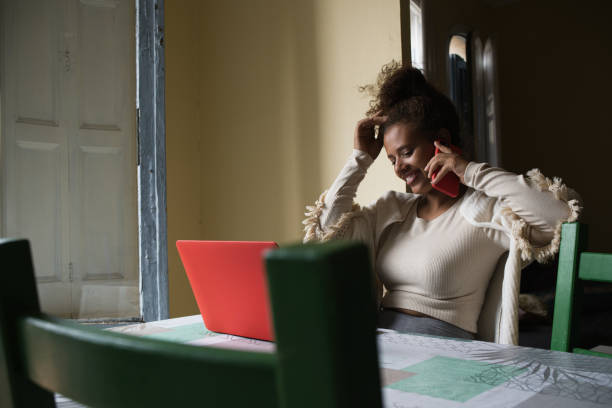 istock Woman talking on the phone while working with a laptop at home. 1352601241