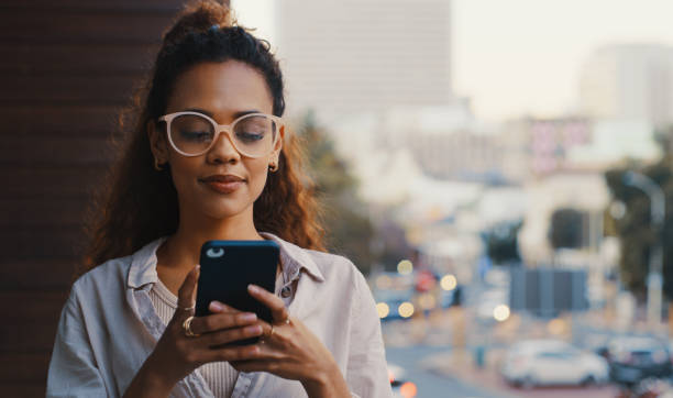 scatto di un'attraente giovane imprenditrice che manda messaggi mentre si trova fuori sul balcone dell'ufficio - smart phone text messaging mobile phone telephone foto e immagini stock