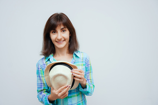 Young smiling brunet caucasian woman taking off hat and loking to camera isolated on gray background