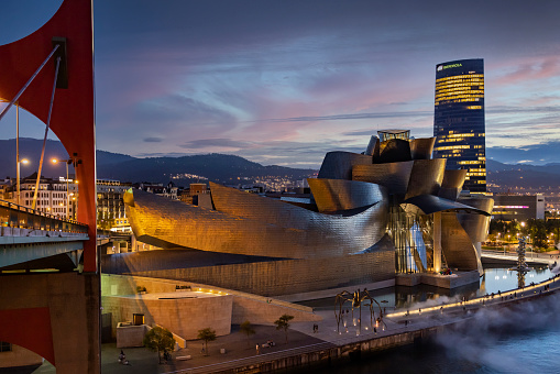 Bilbao, Spain - 8 September 2021: View from La Salve Bridge of Frank Gehry’s avant-garde design on Nervión estuary with city and Basque Mountains in background.