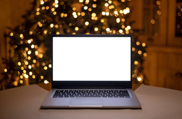 istock Front view of white screen laptop in home with christmas tree warm light. Remote work. Black Friday discounts. Online shopping. Gifts for the new year and christmas. 1352606158