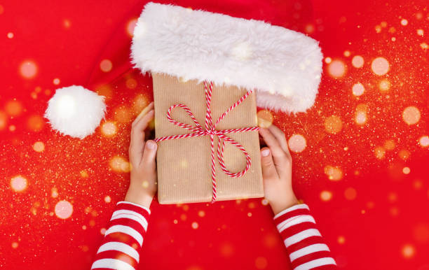 weihnachtsbanner-geschenkbox in kinderhänden auf rotem hintergrund, die ein geschenk präsentiert - 1 2 months stock-fotos und bilder