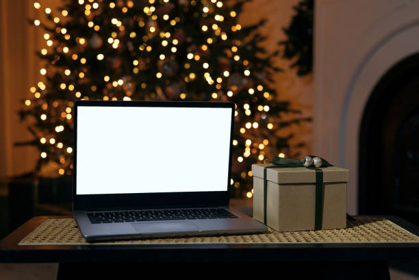 istock Front view of laptop with white screen in home with Christmas tree warm light and gift box. Black Friday discounts. Online shopping. Gifts for the new year and christmas. 1352613499
