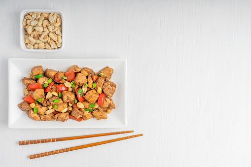 Top view of Kung Pao chicken also Gong Bao a spicy stir-fried Chinese dish made with cubes of chicken, peanuts, vegetables and red peppers served on plate with chopsticks. Image with copy space