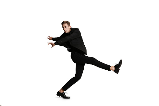 Young man in black business suit dancing isolated on white background. Art, motion, action, flexibility, inspiration and ad concept. Flexible caucasian ballet, contemporary dancer weightless moves