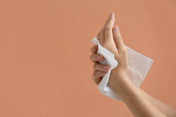 istock Woman cleaning hands with paper tissue on light brown background, closeup. Space for text 1352617813