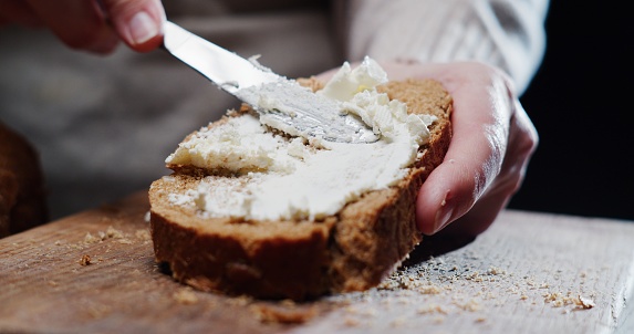 Human hands are spreading cream cheese on a slice of bread