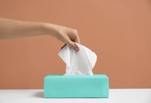 istock Woman taking paper tissue from box on light brown background, closeup 1352619943
