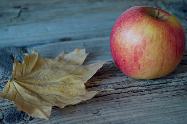istock apple and yellow autumn leaf on old textured wood background 1352620047