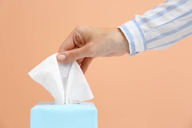 istock Woman taking paper tissue from box on light brown background, closeup 1352621202