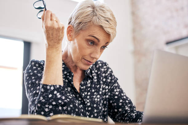 istock Shot of a mature woman sitting alone and feeling stressed while using her laptop to work from home 1352622889