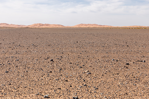 Desolate stone desert in front of the sand dunes of Erg Chebbi in the foreground