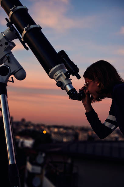 istock Girl with astronomical telescope stargazing under twilight sky. 1352623329