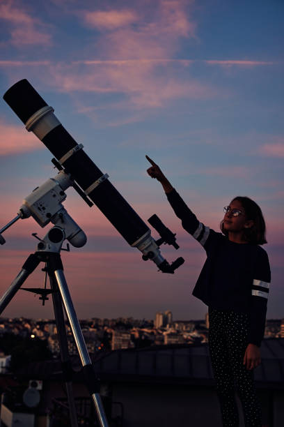 istock Girl with astronomical telescope stargazing under twilight sky. 1352623463