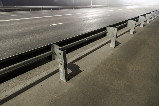 illuminated empty foggy night road with rigid guardrails, traffic barriers or crash barriers