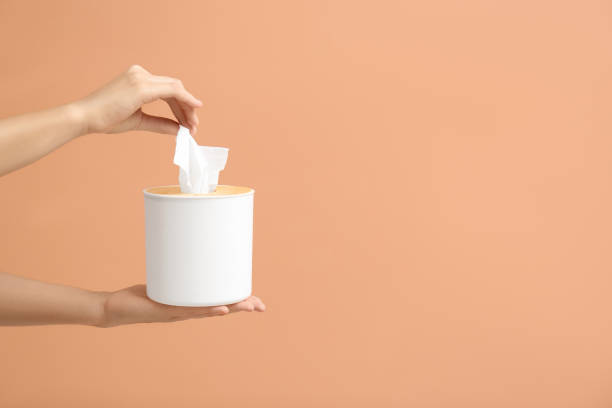 istock Woman taking paper tissue from holder on light brown background, closeup. Space for text 1352624736