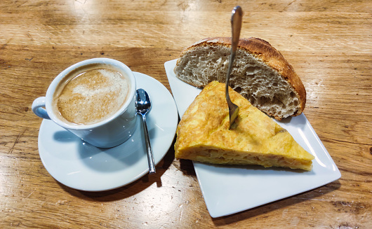 Coffee with milk and delicious skewer of potato or Spanish omelette with loaf of bread