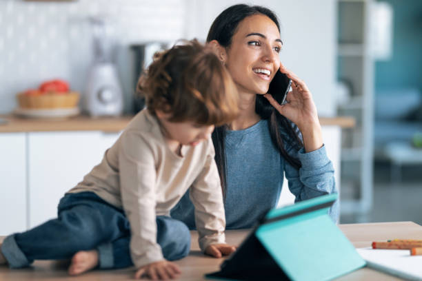 istock Young smiling mother and her cute son watching cartoons on digital tablet while talking with smartphone in the kitchen at home. 1352643716