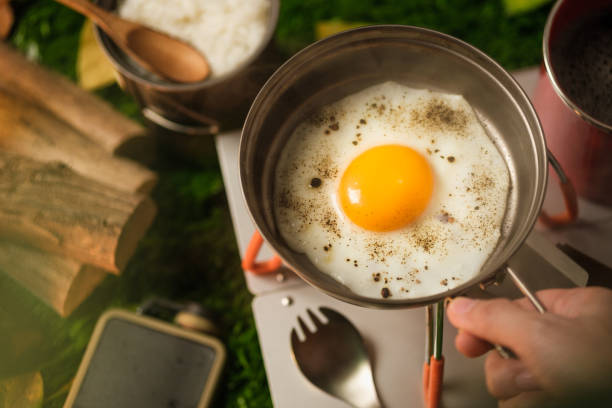 close up hand fried egg on pan when camping in holiday vacation stock photo