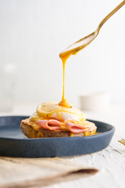 egg Benedict with hollandaise sauce on dark blue plate on table in kitchen egg Benedict with hollandaise sauce on dark blue plate on table in kitchen hollandaise sauce stock pictures, royalty-free photos & images
