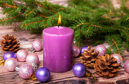 Christmas composition of a burning candle, christmas balls, cones and a spruce branch on a wooden table