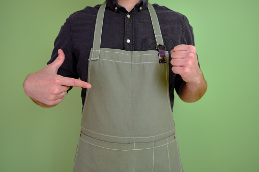 A man in a kitchen apron. Chef work in the cuisine. Cook in uniform, protection apparel. Job in food service. Professional culinary. Green fabric apron, casual stylish clothing. Handsome baker posing