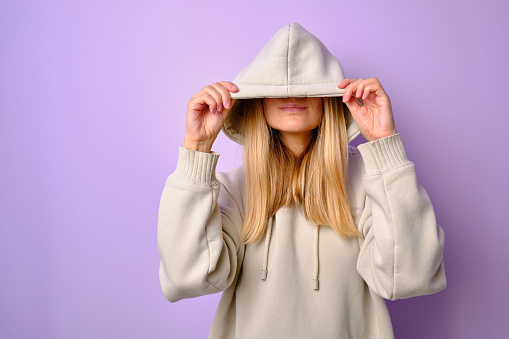 Young beautiful girl in a white hoodie posing. Warm oversized hoodie with an hood. Stylish trendy hipster bow. Trying on clothes in a store. Youth subculture. Fashion clothing advertising