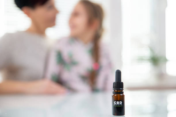 CBD Oil Bottle on Table With Mother and Daughter in Background stock photo