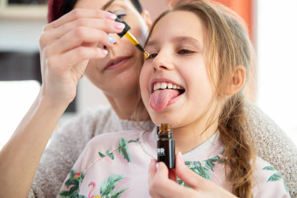 Daughter Sticking Out Tongue To Mother Can Drop CBD Oil Drops on It stock photo