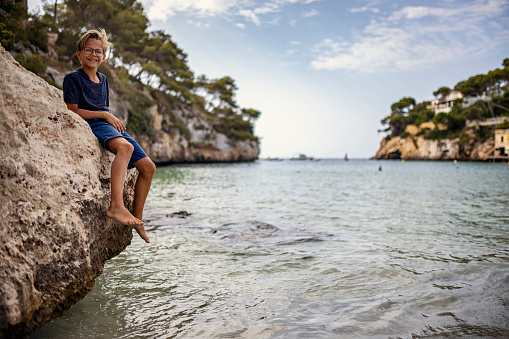 Teenage boy enjoying sunny vacations day. The boy is sitting on rocks of the beautiful cove on the shores of Majorca, Spain.
Canon R5