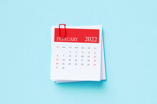 2022 February calendar attached with a red paperclip sitting on aquamarine background. Horizontal composition with copy space. Directly above. Calendar and reminder concept.