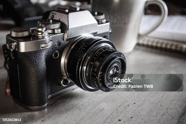 Antique Old 50mm Ussr Lens From The 70s On A Silver And Black Hybrid Camera Body On A Grey Desk Top With Coffee Mug Stock Photo - Download Image Now