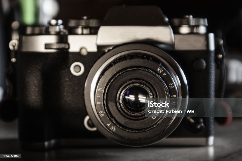 Close up view of a vintage old 50mm USSR lens on a silver and black hybrid camera body on a grey desk top Studio pictures of an old vintage 50 mm USSR lens on a silver and black hybrid camera body on a grey desk top in a dark environment. Aluminum Stock Photo