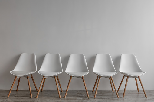 Row of five white chairs on gray wall background in office or living room, nobody. Modern interior, minimalist design, scandinavian style. Recruiting, self-isolation crisis due covid-19 quarantine