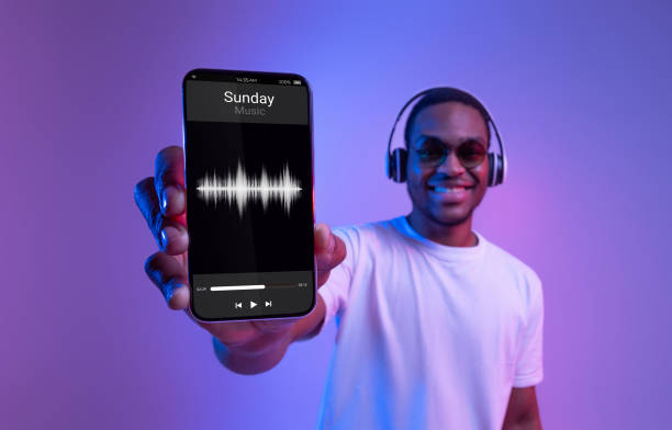 Music App. Cheerful Black Guy In Wireless Headphones Showing Smartphone With Audio Player Interface On Screen, African Man Enjoying Favorite Playlist, Standing Under Purple Neon Light, Collage