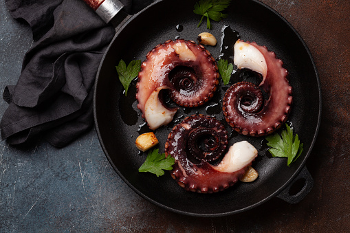 Grilled octopus with herbs and spices on frying pan. Top view flat lay