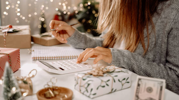 Girl counting US Dollar bills, using calculator, and writing expenses. Woman doing budget, estimating money balance for shopping spree. Female accountant paying taxes. Girl counting Christmas gifts. chica contando billetes de dólares estadounidenses, usando calculadora y escribiendo gastos. mujer haciendo presupuesto, estimando el saldo de dinero para la juerga de compras. mujer contadora pagando impuestos. chica contando regalos de navidad