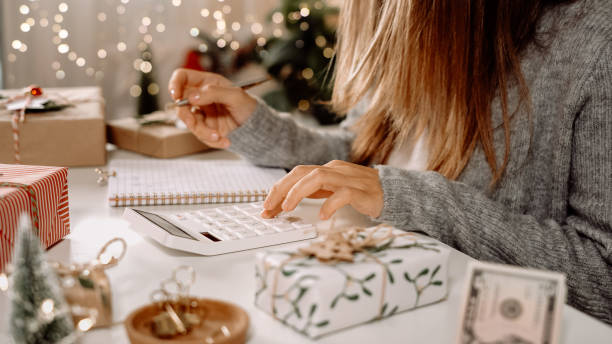 Girl counting US Dollar bills, using calculator, and writing expenses. Woman doing budget, estimating money balance for shopping spree. Female accountant paying taxes. Girl counting Christmas gifts Girl counting US Dollar bills, using calculator, and writing expenses. Woman doing budget, estimating money balance for shopping spree. Female accountant paying taxes. Girl counting Christmas gifts. budget stock pictures, royalty-free photos & images