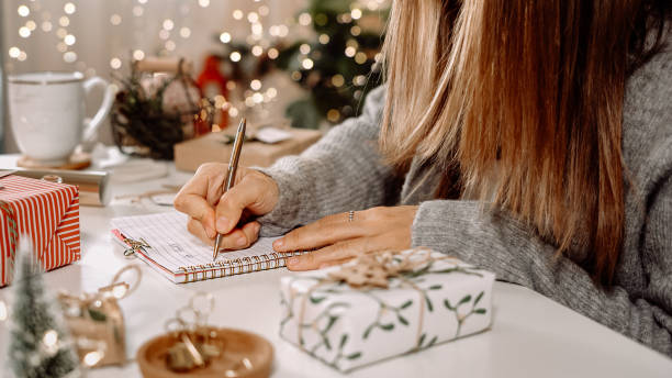 Goals plans make to do and wish list for new year christmas concept, girl writing in notebook. Woman hand holding pen on notepad at home on winter holidays xmas. Christmas decoration, gift boxes. metas que los planes hacen para hacer y lista de deseos para el concepto de navidad de año nuevo, niña escribiendo en cuaderno. mujer de la mano sosteniendo el bolígrafo en el bloc de notas en casa en las vacaciones de invierno navidad. decoración navi