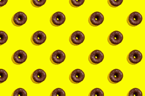 istock Flat lay pattern of tasty chocolate donut on yellow background. 1352659094