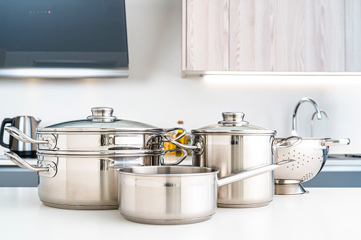 Set of stainless steel cooking pots shot on modern kitchen countertop. High resolution 42Mp indoors digital capture taken with SONY A7rII and Zeiss Batis 40mm F2.0 CF lens