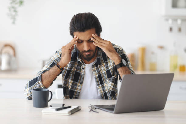 istock Exhausted man sitting in front of laptop, touching his head 1352660895