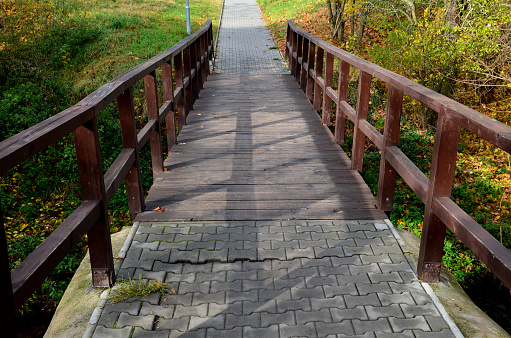 pedestrian bridge over a small gorge and a stream. it consists of two steel crossbeams. as the surface and railing of the bridge is made of brown painted planks. is long and narrow. in the wild, crossbeam, foundation, gorge