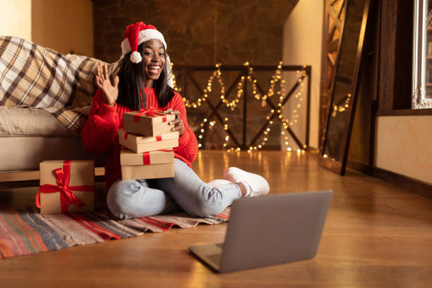 istock Excited young black lady with gift boxes making video call on laptop, waving at webcam, greeting friends with Christmas 1352662061
