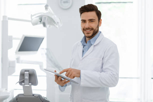 attractive man dentist with digital tablet smiling at camera - dentist imagens e fotografias de stock